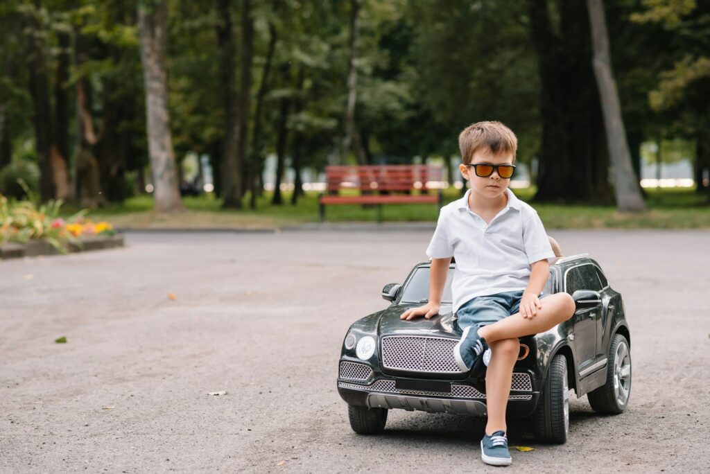 Cute boy in riding a black electric car in the park. Funny boy rides on a toy electric car
